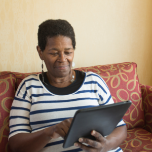 Picture of an older woman sitting on a couch and touching an iPad screen