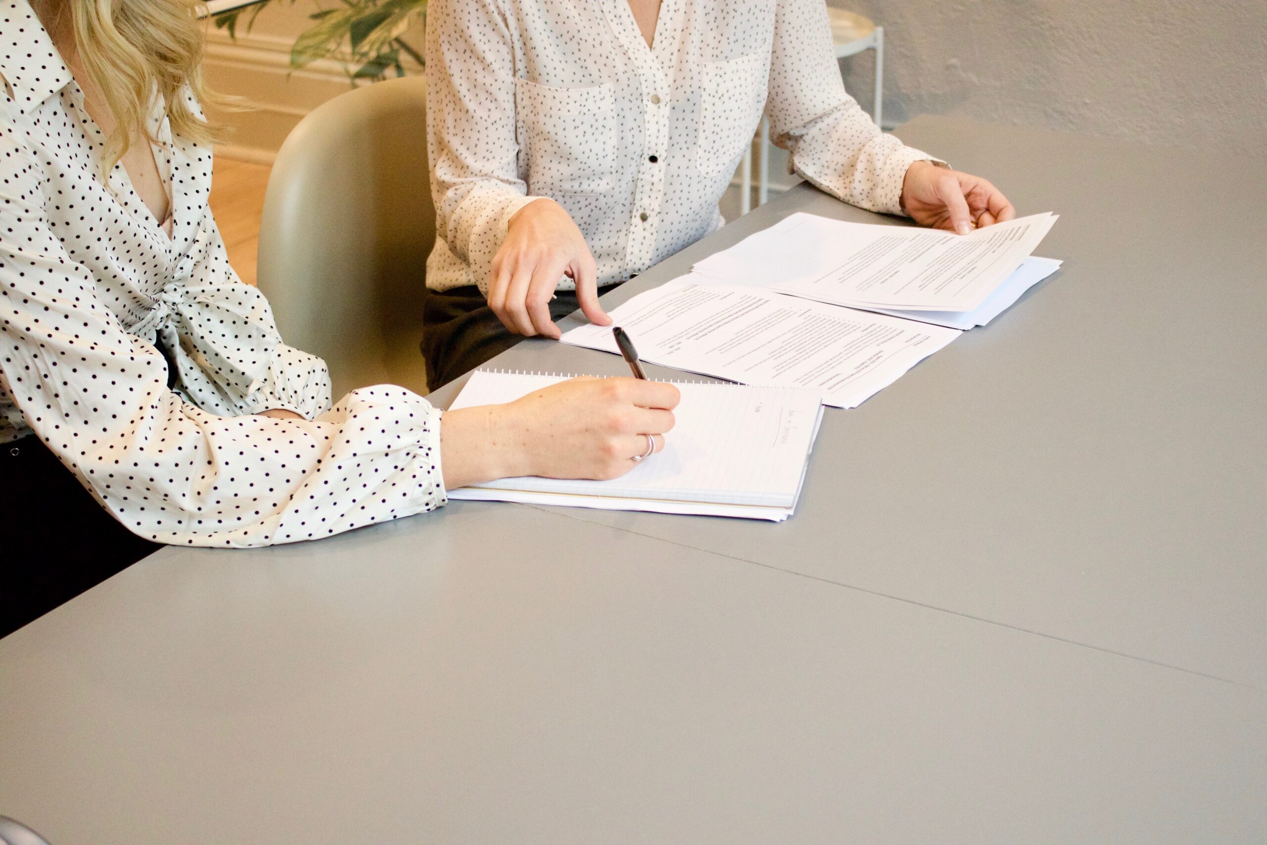 view of two women sitting at a table signing paperwork. faces not visible.