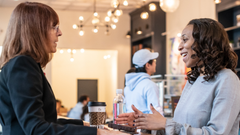 two businesswomen talking at high top table in a coffee shop