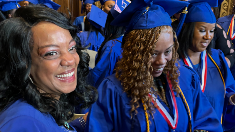 Woman smiling with high school graduates dressed in cap and gown.