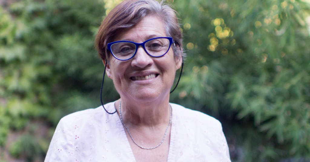 Image description. Older woman wearing glasses and a white shirt smiles at the camera for Career Solutions for 55+. End description.