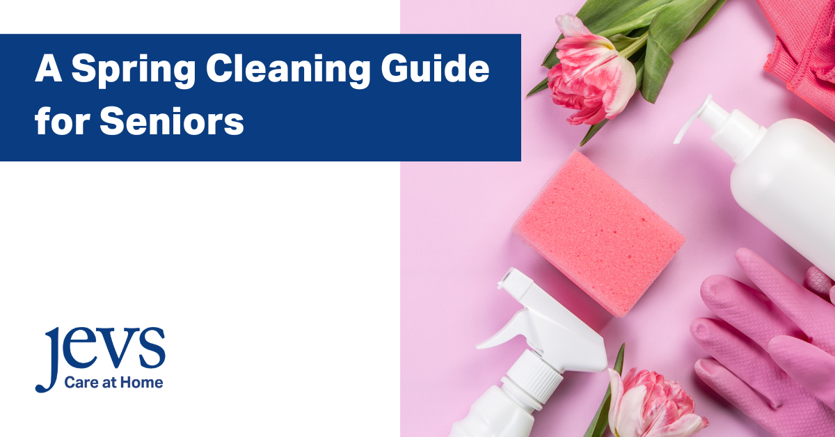 Image description: One picture of a white background with the JEVS Care at Home logo in the lower left corner. The top left corner has a navy blue rectangle with letters in white on it that say: A Spring Cleaning Guide for Seniors. An image on the right side of the picture has a light pink background and the following items in front of the pink background: a pink flower, a pair of dark pink gloves, a white bottle with a pump, light pink gloves, another flower, and a white spray bottle. End description.