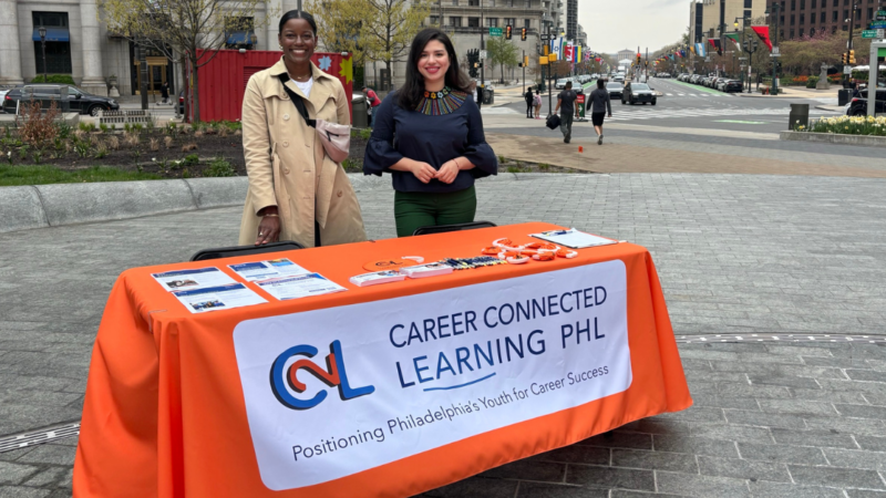 Image description. Two women standing behind a display table advertising paid learning experiences for youth and young adults and that presents this text: C2L Career Connected Learning PHL. Positioning Philadelphia's Youth for Career Success. End description.