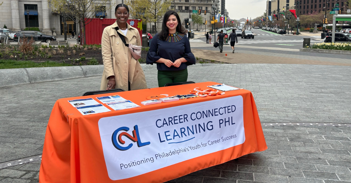 Image description. Two women standing behind a display table advertising paid learning experiences for youth and young adults and that presents this text: C2L Career Connected Learning PHL. Positioning Philadelphia's Youth for Career Success. End description.