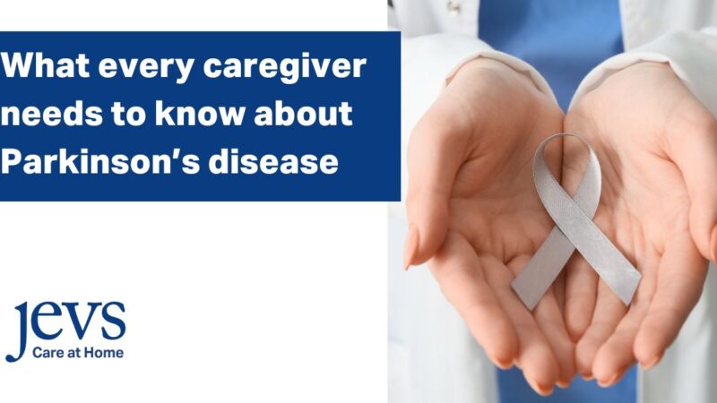 Image description. Banner in the top left corner has a blue background with text in white letters that say: What every caregiver needs to know about Parkinson's disease. Logo in bottom left corner says: JEVS Care at Home. Picture on right side of image is of two open, palms-up hands holding a silver ribbon that represents Parkinson's disease awareness. End description.