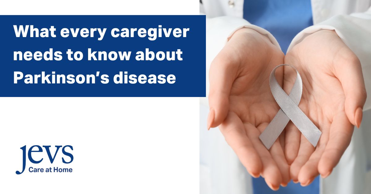 Image description. Banner in the top left corner has a blue background with text in white letters that say: What every caregiver needs to know about Parkinson's disease. Logo in bottom left corner says: JEVS Care at Home. Picture on right side of image is of two open, palms-up hands holding a silver ribbon that represents Parkinson's disease awareness. End description.