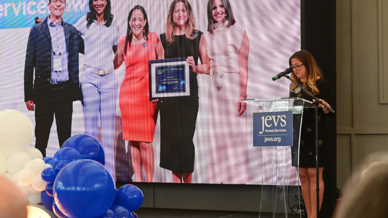 Image Description. JEVS' President and CEO, Cynthia Figueroa, stands in front of screen and gives a speech. End description.