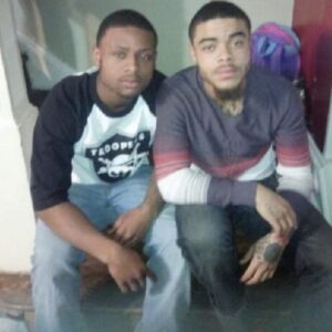Image of two young men sitting by each other at the bottom step of a staircase in a home.