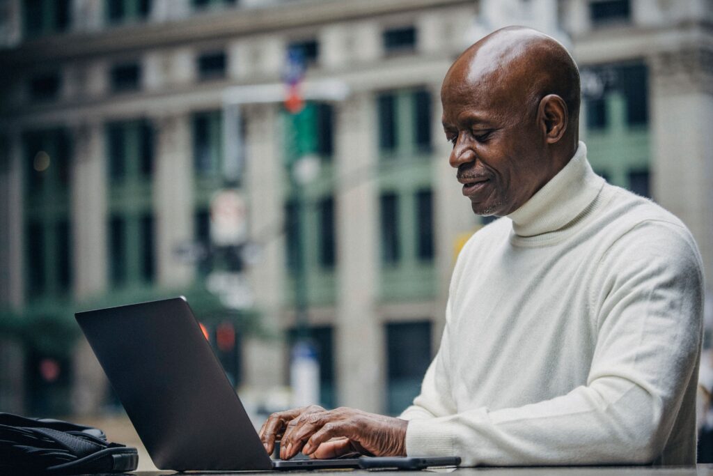 A man works on a laptop in an outdoor location in a city.