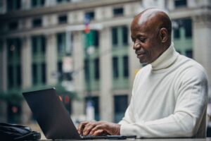 A man works on a laptop in an outdoor location in a city.