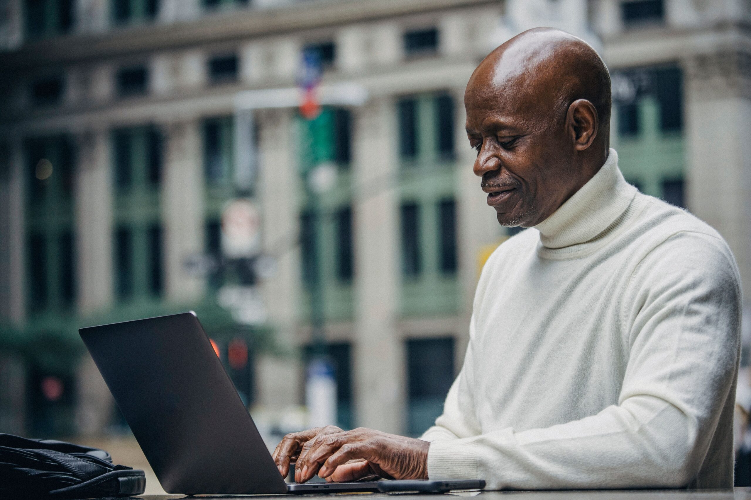 A man works on a laptop in an outdoor location in a city.