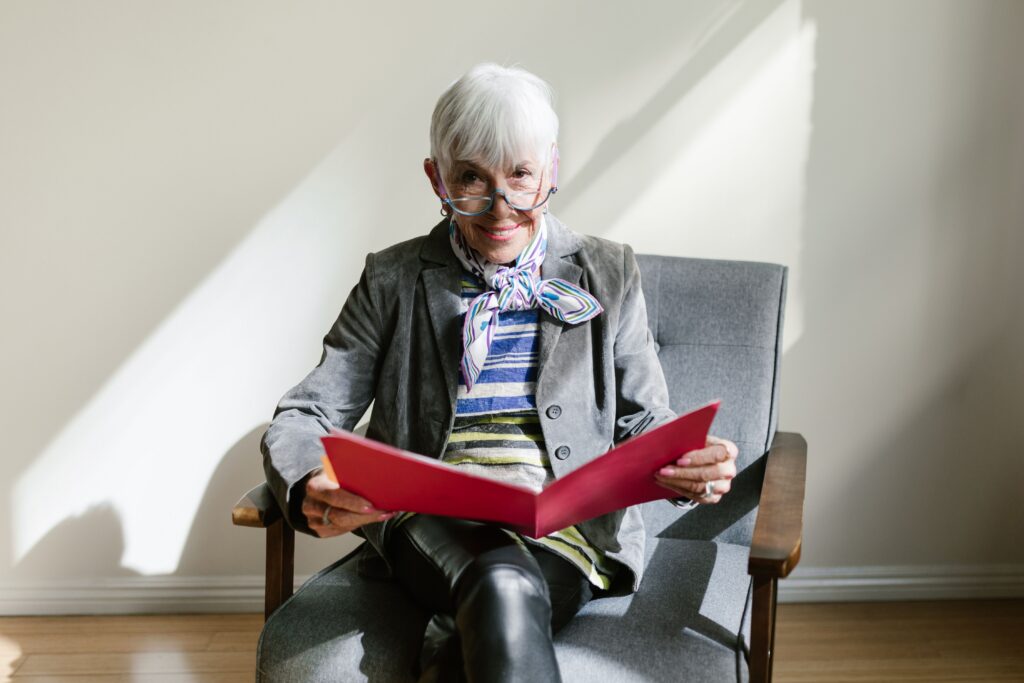 A woman who is over 55 sits in a chair holding an opened folder and smiling.